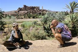 Image du Maroc Professionnelle de  Le paysage, formé par la kasbah Tifoultoute  qui se dresse majestueusement sur un éperon rocheux qui domine la vallée de l'oued Ouarzazate, attire les touristes qui prennent le temps de s'arrêter pour prendre une photo. Précisément à cet endroit un charmeur de serpent tenant une vipère avec sa main gauche tout en surveillant le mouvement du scorpion noir qu’il avait accroché à son cou avec sa main droite pose aux touristes contre un billet avec derrière lui comme décor celui qui avait servit pour de grand films comme Lawrence d’Arabie et Jésus de Nazareth à quelque kilomètres de la ville de Ouarzazate au sud du Maroc le Samedi 23 Août 1997. (Photo / Abdeljalil Bounhar)
 